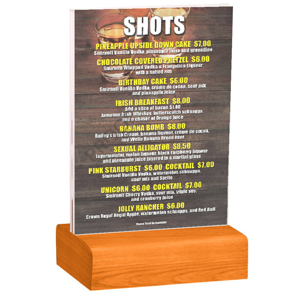 A Menu Solutions clear acrylic table tent with solid wood base holding a drink menu on a wood table.