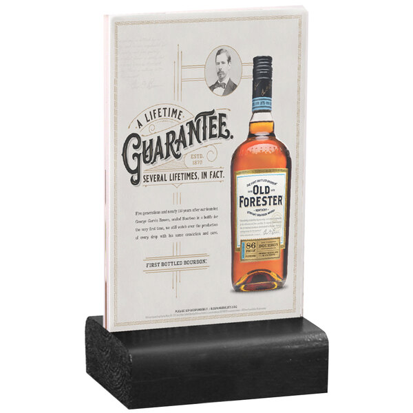 A Menu Solutions clear acrylic table tent with a black wood base holding a whiskey bottle on a table.