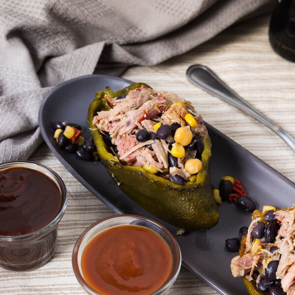 A plate with two stuffed Del Sol whole poblano peppers with meat and corn on a plate with sauce.