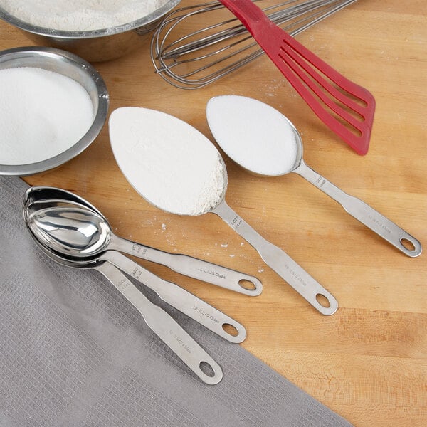 A Thunder Group stainless steel measuring scoop set with measuring spoons and a spoon of white powder.