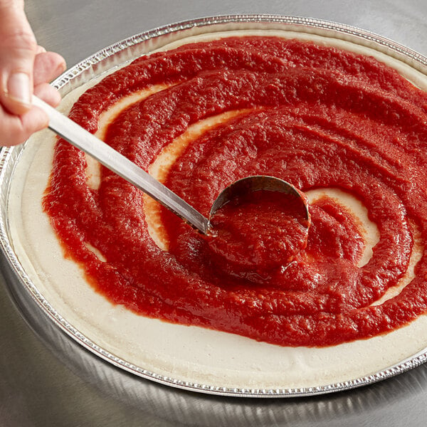 A person using a spoon to spread Furmano's pizza sauce on a pizza.