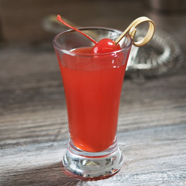 A Libbey Flare shooter glass filled with red liquid and a cherry on top.