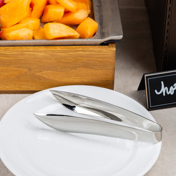 American Metalcraft stainless steel serving tongs on a plate of fruit on a hotel buffet table.