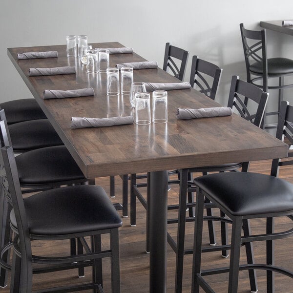 A Lancaster Table & Seating wood butcher block table with espresso finish on a table in a restaurant dining area with black leather chairs.