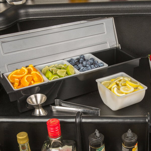 A black condiment dispenser insert with a red cap on a counter with bowls of fruit slices.