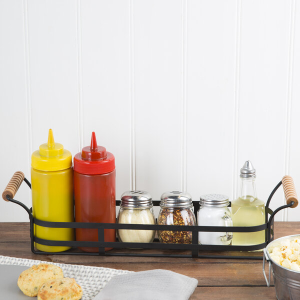 A Tablecraft black metal condiment caddy with red and yellow condiment containers and a glass jar with a metal lid.