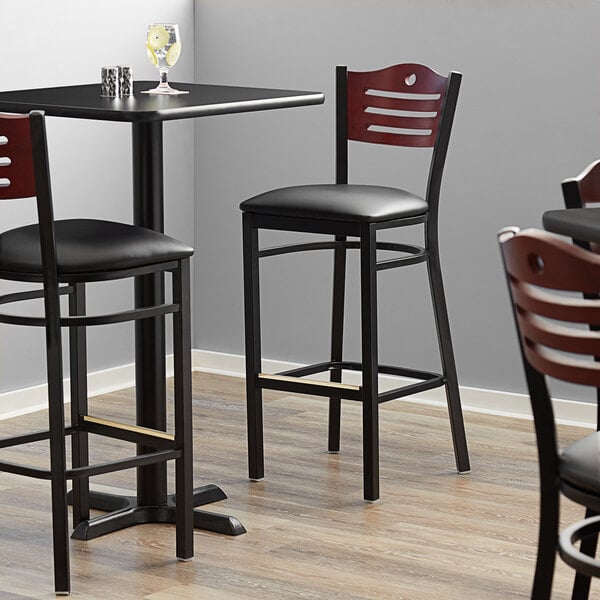 A Lancaster Table & Seating black bistro bar stool with black vinyl seat and mahogany wood back.
