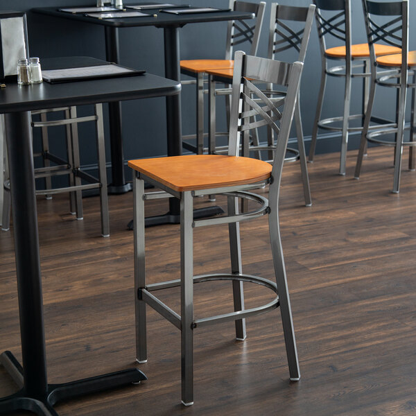 A Lancaster Table & Seating cross back bar stool with a cherry wood seat on a table in a restaurant dining area.