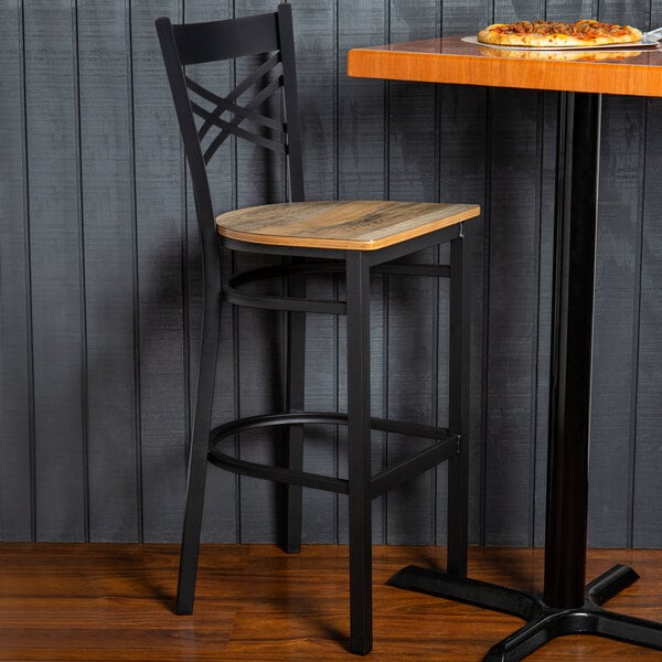 A Lancaster Table & Seating black finish cross back bar stool with a wooden seat at a table with pizza on it.