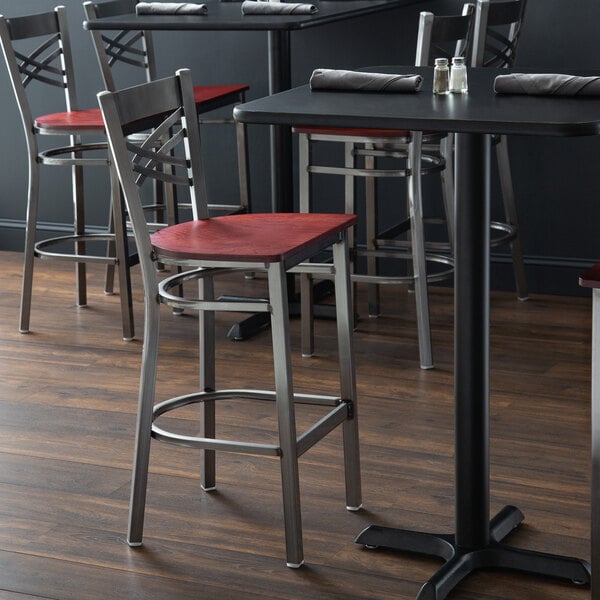 A Lancaster Table & Seating cross back bar stool with a mahogany wood seat on a table in a restaurant dining area.