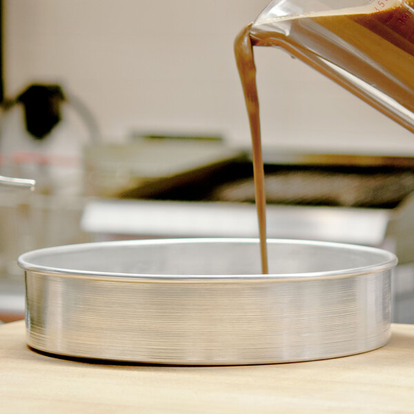 A person pouring liquid into an American Metalcraft aluminum round cake pan.