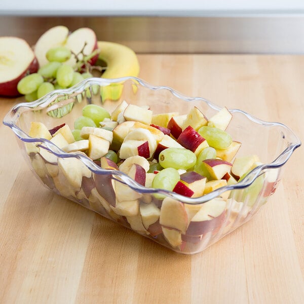 A Cambro clear deli crock filled with fruit on a table.