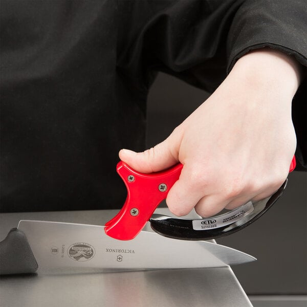 A person using a Chef Master carbide knife sharpener to sharpen a red-handled knife.