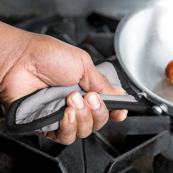 A hand using a gray silicone pot handle cover on a frying pan.