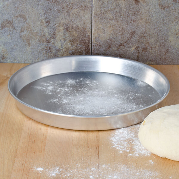 An American Metalcraft aluminum pizza pan with flour on it next to a ball of dough.