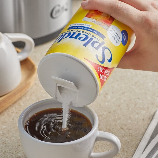 A hand pouring Splenda sweetener into a white cup of coffee.