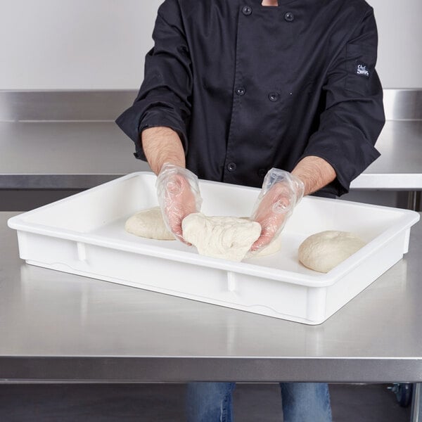 A man in a chef's uniform using a white Cambro pizza dough proofing box to hold white dough.