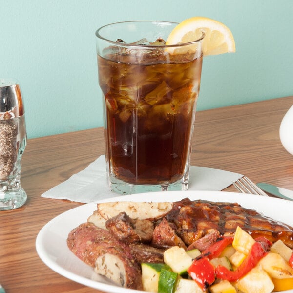A Libbey Gibraltar beverage glass filled with ice tea on a table with a plate of food.