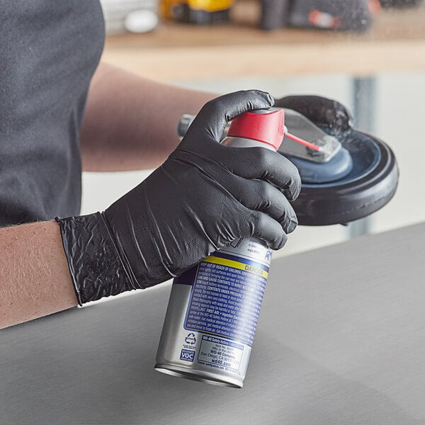 A person wearing Lavex Pro black nitrile gloves holding a spray can.