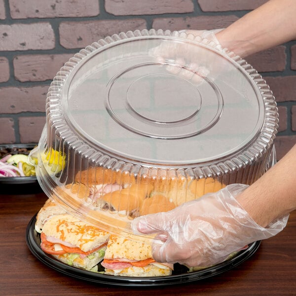A person putting a sandwich in a Sabert plastic container.