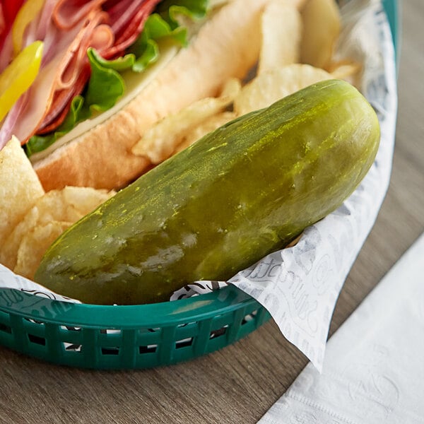 A B&G whole kosher dill pickle next to a sandwich on a plate.