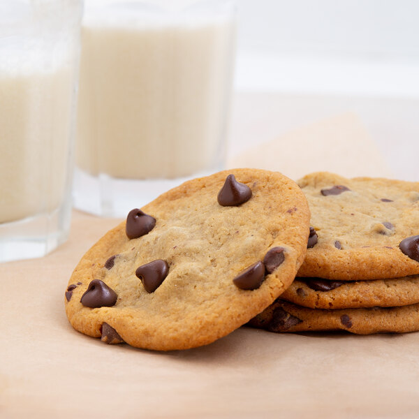A stack of chocolate chip cookies with a glass of milk on a table.