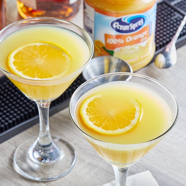 Two glasses of orange juice with orange slices on top.