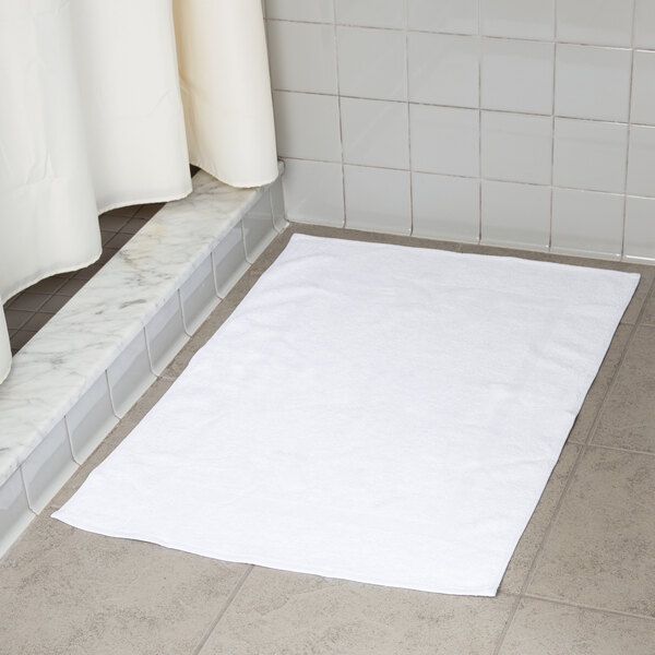 A white Oxford bath mat on a white tile floor.