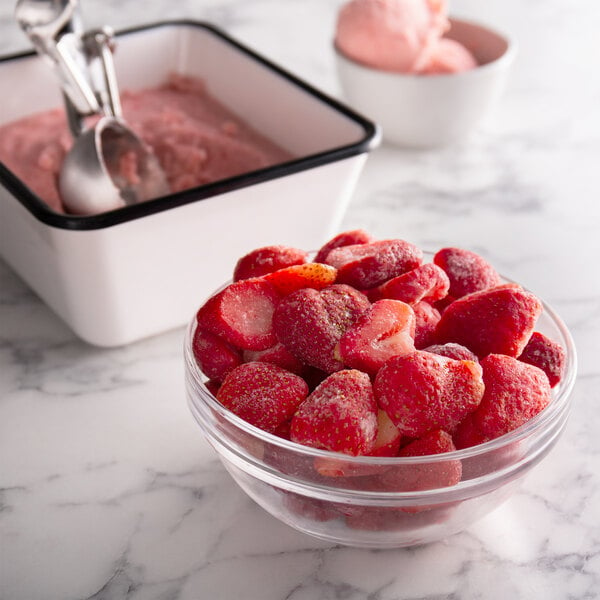 A bowl of sliced strawberries next to a bowl of pink ice cream.