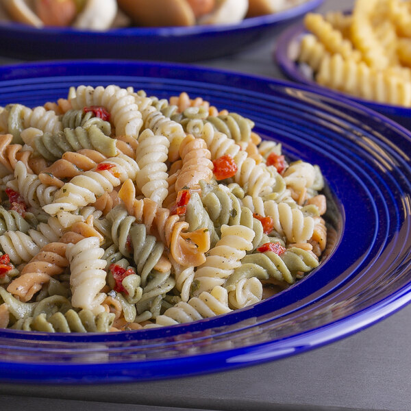 A blue plate with Spring Glen Fresh Foods Rotini Pasta Salad with different colored spirals on a table in a salad bar.