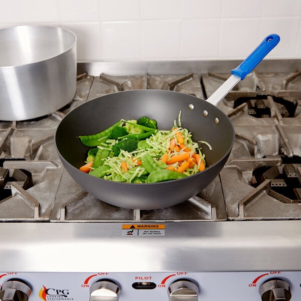 A Vollrath Wear-Ever stir fry pan with vegetables in it on a stove.