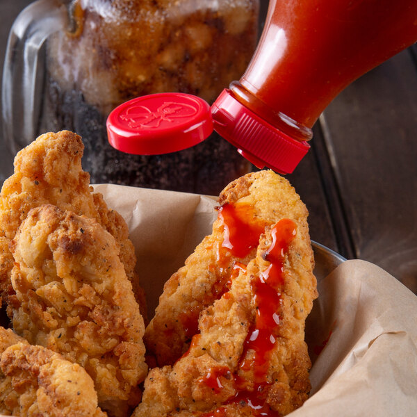 A person pouring Texas Pete Original Hot Sauce on fried chicken.