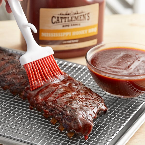 A hand using a brush to spread Cattlemen's Mississippi Honey BBQ Sauce on ribs.