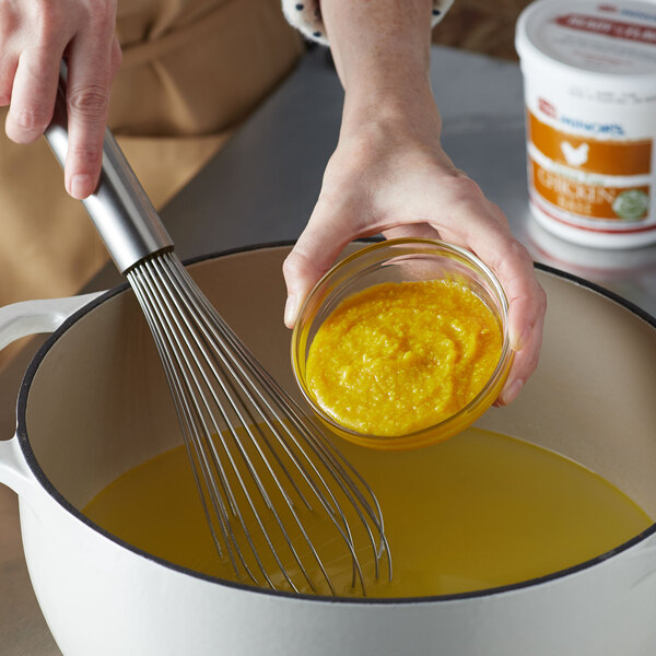 A person using a whisk to stir yellow liquid in a bowl.