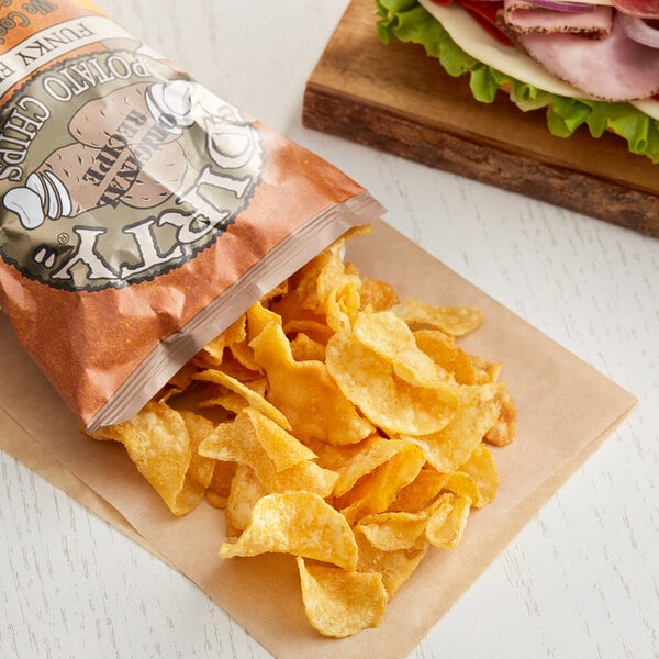 A bag of Dirty Potato Chips Funky Fusion next to a sandwich on a table.