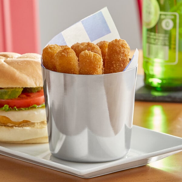 A silver container full of french fries on a table with a burger.