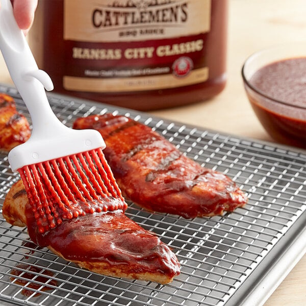 A person brushing Cattlemen's Kansas City Classic BBQ sauce on meat.