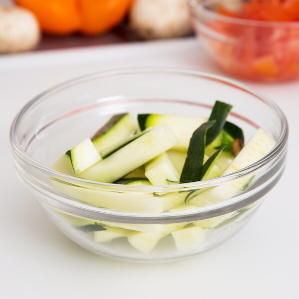An Arcoroc glass bowl filled with sliced zucchini and cucumbers.