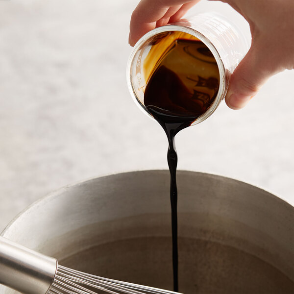 A hand pouring brown liquid from a Kitchen Bouquet jar into a bowl.
