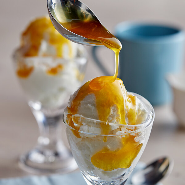A spoon is pouring J. Hungerford Smith butterscotch topping over a bowl of ice cream.