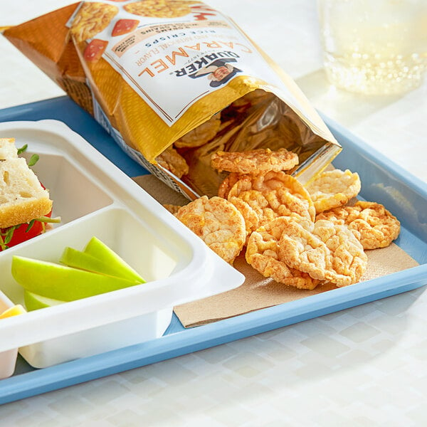A white container with Quaker Caramel Corn Popped Rice Crisps on a table of food.