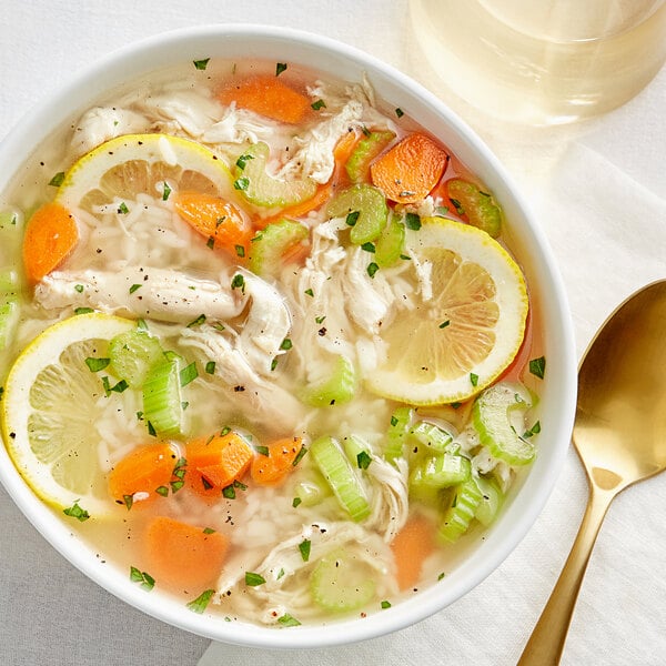 A bowl of Swanson chicken soup with vegetables and lemons.