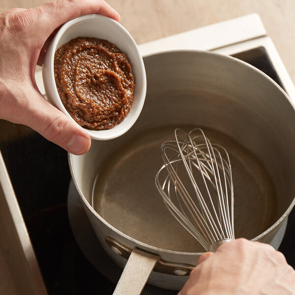 A person stirring a pot of brown Custom Culinary turkey base paste with a whisk.