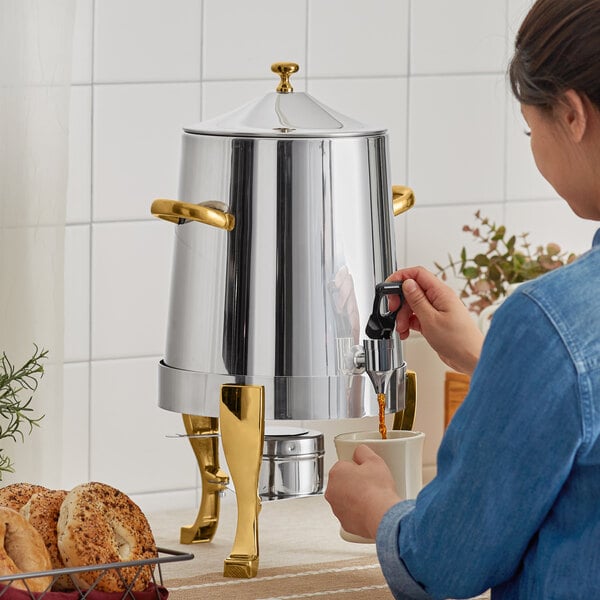 A woman using a Choice Deluxe Stainless Steel Coffee Chafer Urn to pour coffee into a mug.