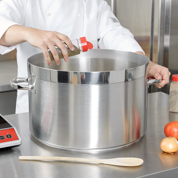 A chef adding seasoning to a Vollrath Centurion sauce pot on a counter.