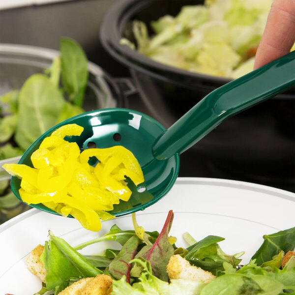 A person using a Thunder Group green perforated salad bar spoon to serve salad with yellow peppers.