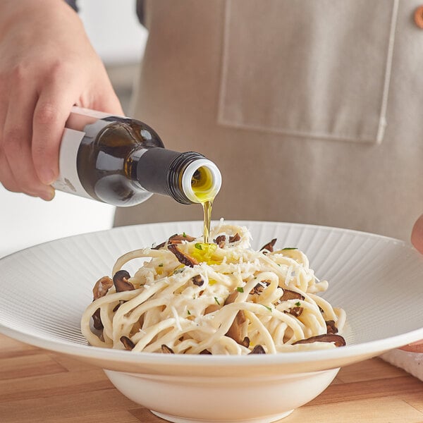 A person pouring white truffle oil onto a bowl of noodles with mushrooms.