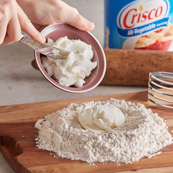 A person putting Crisco into a bowl of flour.