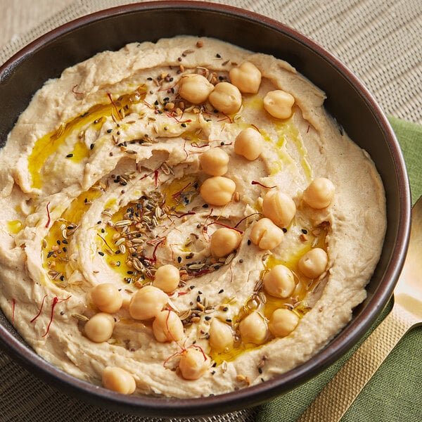 A bowl of hummus with chickpeas and seeds on top.