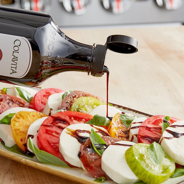 A plate of food with tomatoes, cheese, and balsamic glaze being poured over it from a Colavita Original Balsamic Glaze bottle.